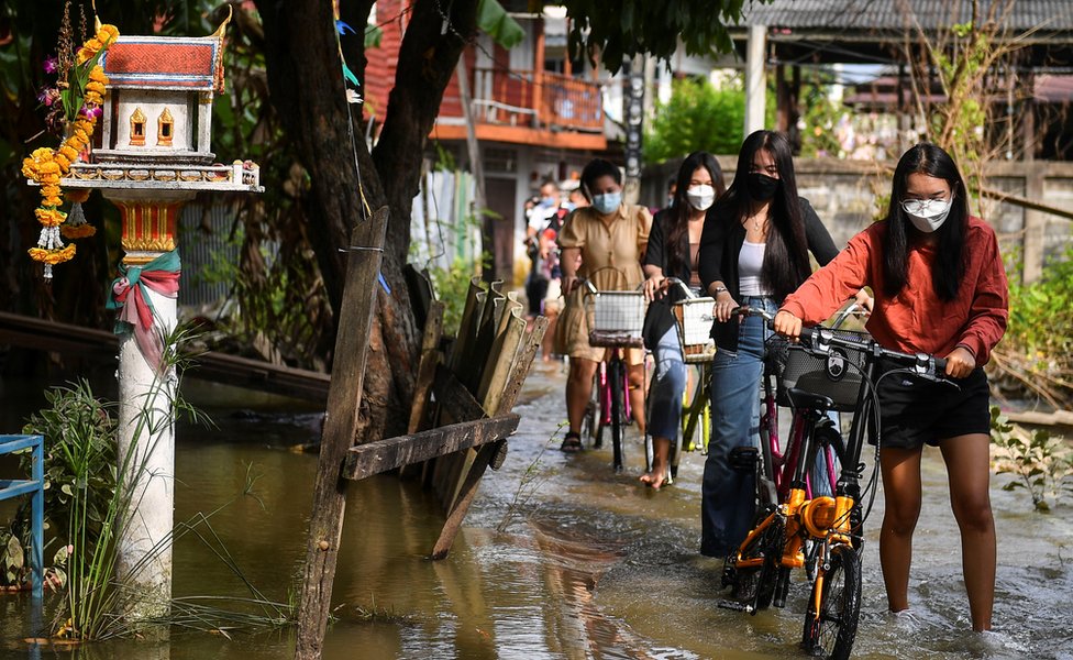 Pipo dey waka through a flooded street wit dia bicycles for Nonthaburi province, on di outskirts of Bangkok