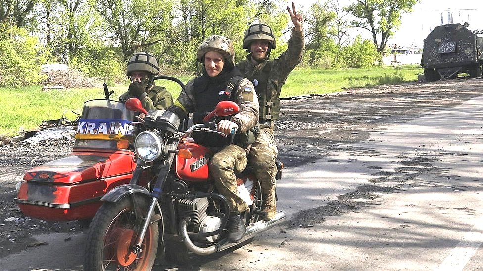 Ukrainian servicemen ride ontop motorcycle on di road wey connect Kharkiv and one village wey Ukrainian Army recently retake