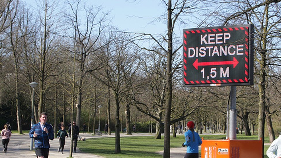 People running pass a sign urging people to practice social distancing in Amsterdam