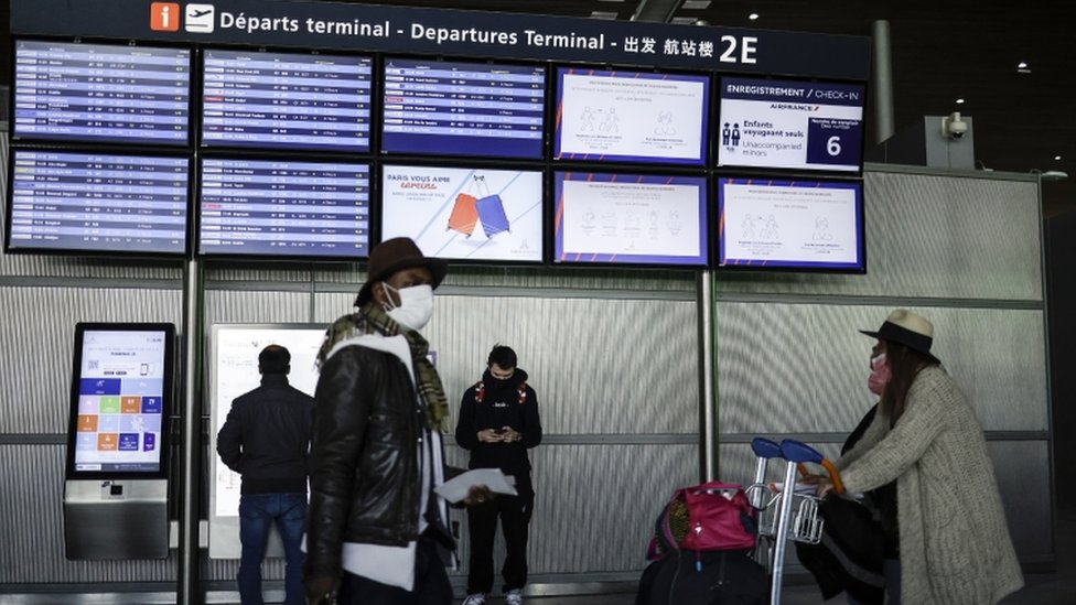 Flight passengers waka next to a Flight Information board for Charles de Gaulle Airport