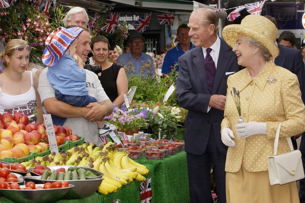 Queen Elizabeth II (right) and di Duke of Edinburgh (centre right) wen dem visit market stalls for Kingston town centre, during di Queen Golden Jubilee visit to West London