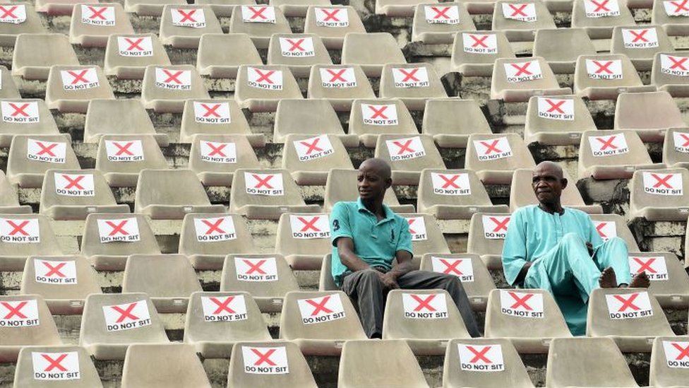 Two men sidon for middle of stadium wey dem mark 'Do Not Sit' ontop chairs