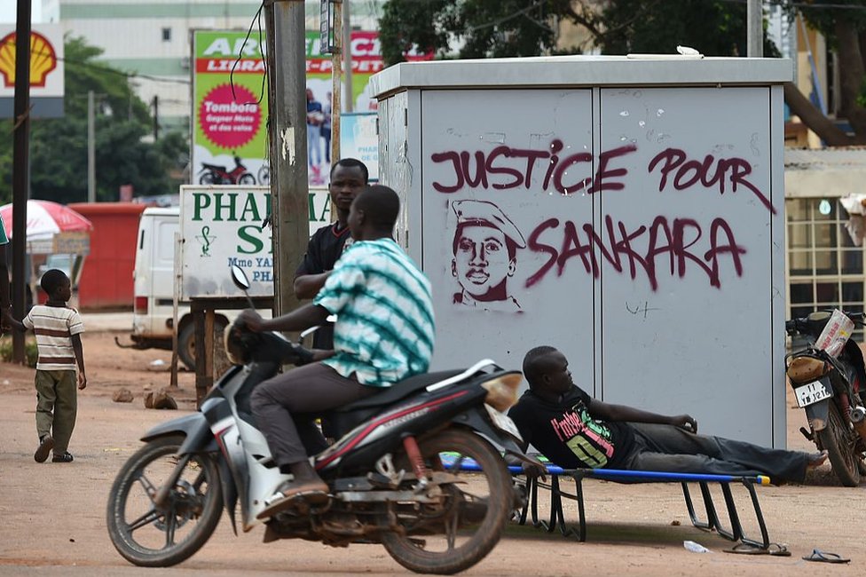 People stand next to graffiti wey read "justice for Sankara".