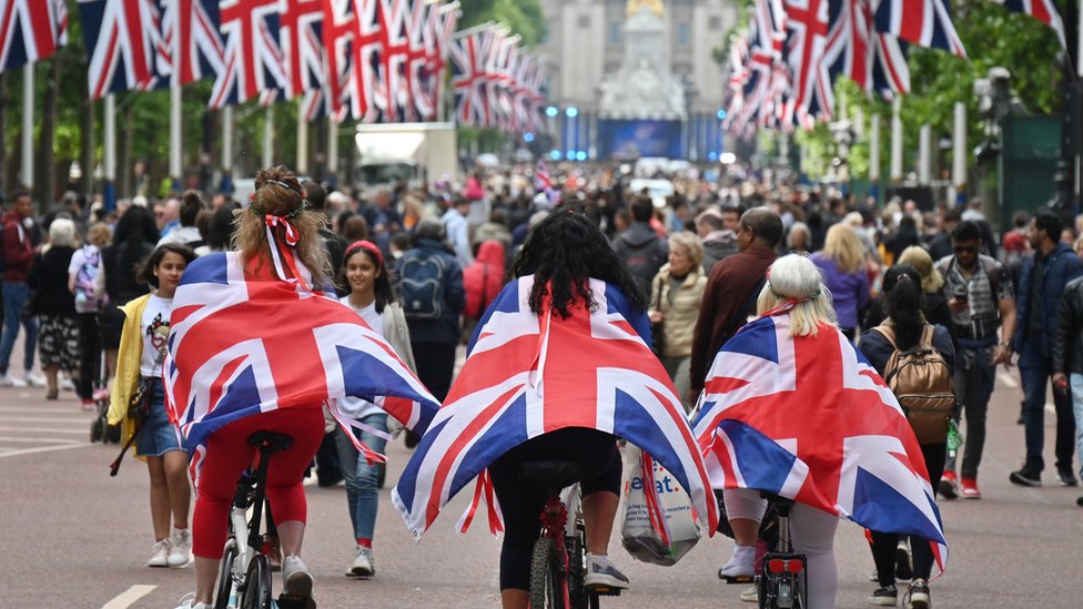 Women wey wear di Union Jack flags as capes, cycle downdi mall towards Buckingham Palace