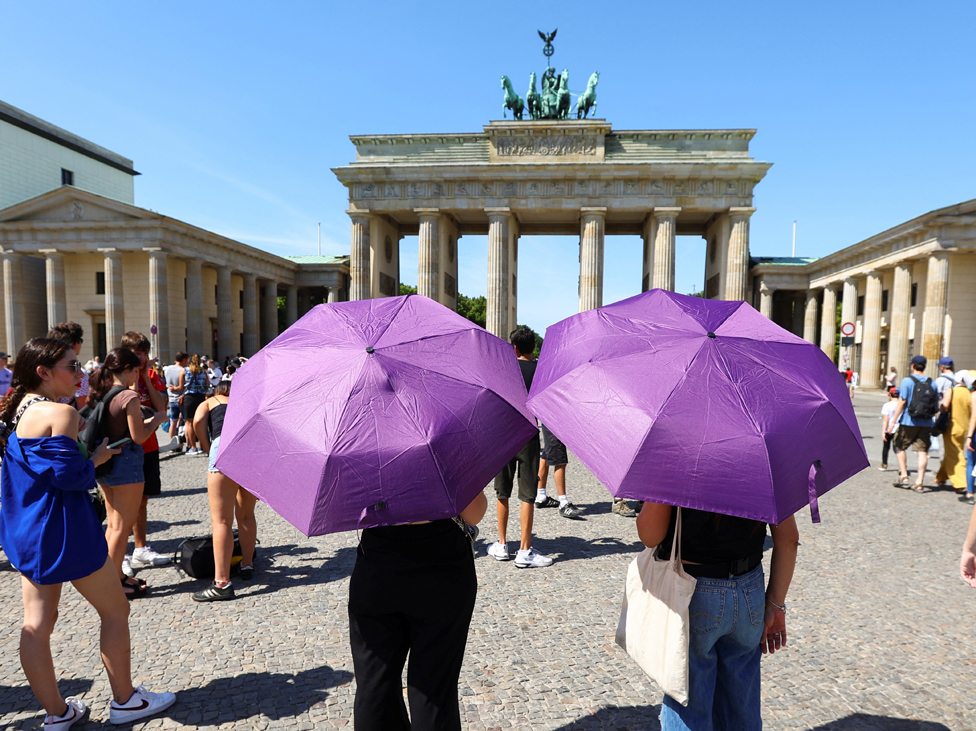 Women shield themselves from sun with umbrellas during a heatwave in front of the Brandenburg Gate in Berlin, Germany,