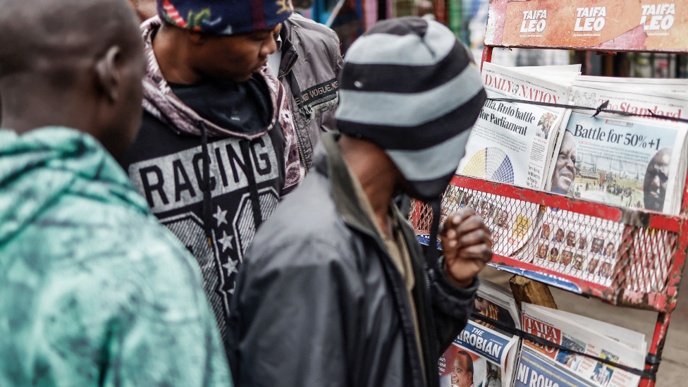 Residents look at newspapers displayed at a stand in Mathare, Nairobi following Kenya's general election on 12 August 2022