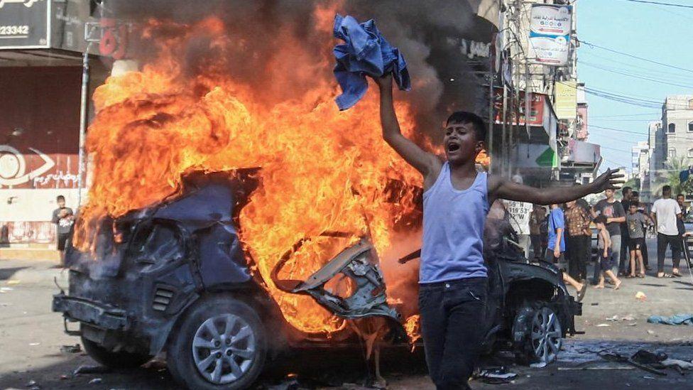 One Palestinian boy react in front of one burning Israeli car wey militants seize