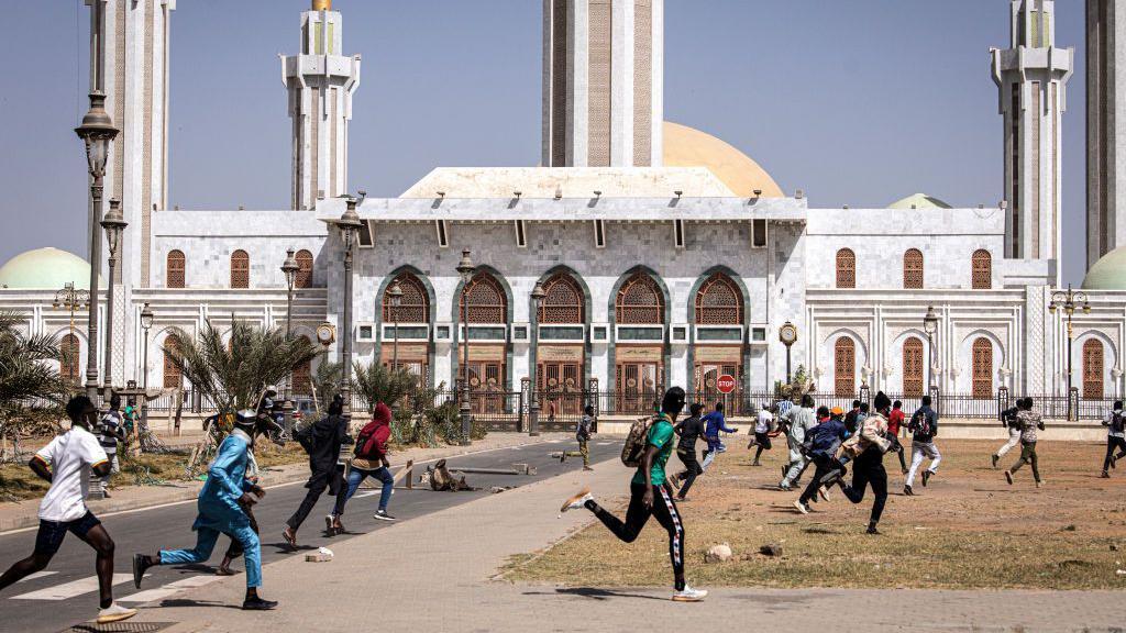 Protesters run past one mosque during gbege with police for Dakar, Senegal - 9 February 2024