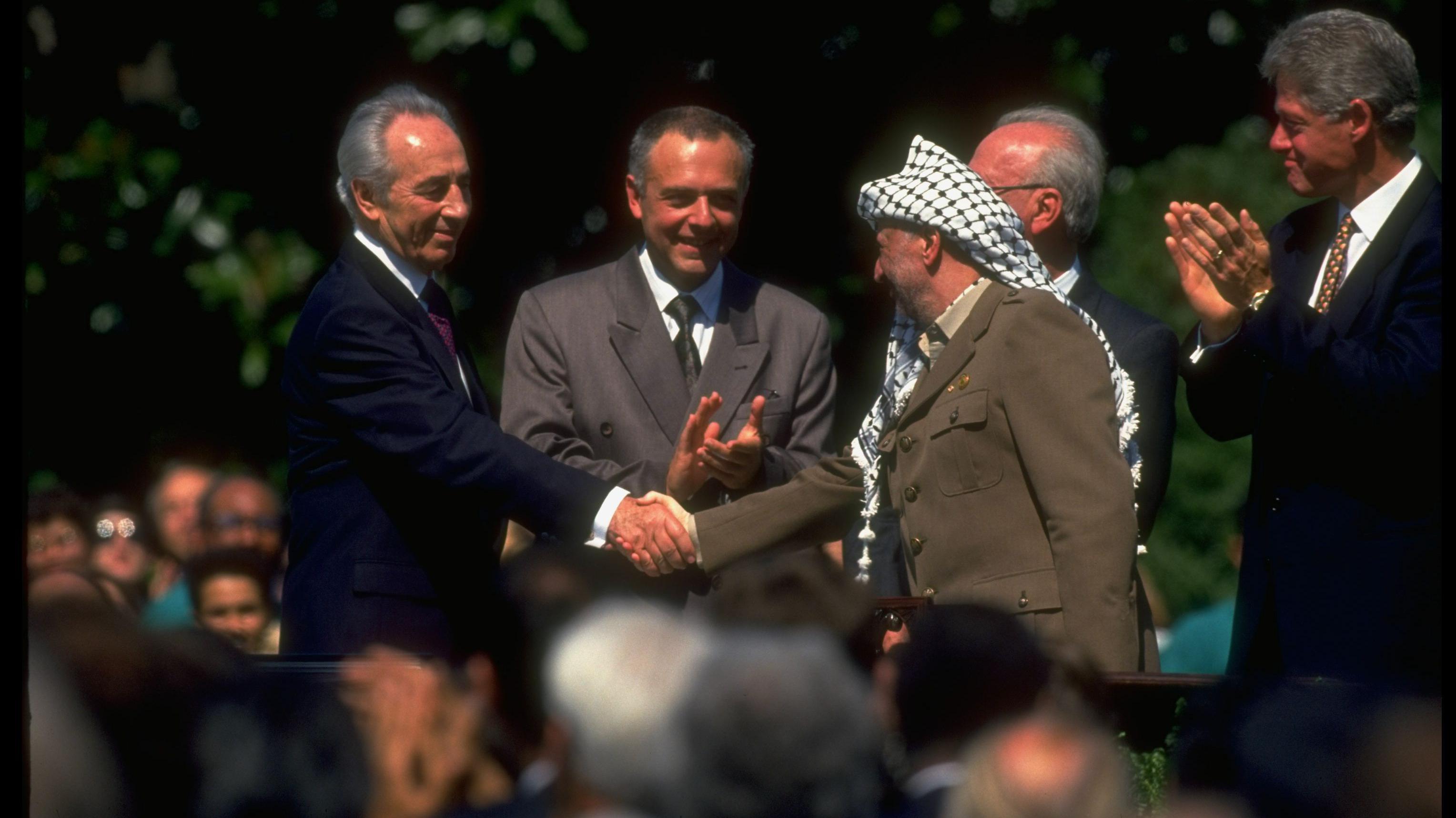 PLO leader Yasser Arafat (Right) dey shake hand wit Israeli foreign minister Shimon Peres for di Oslo Accord signing wit US President Bill Clinton (Far right) wey dey clap im hands