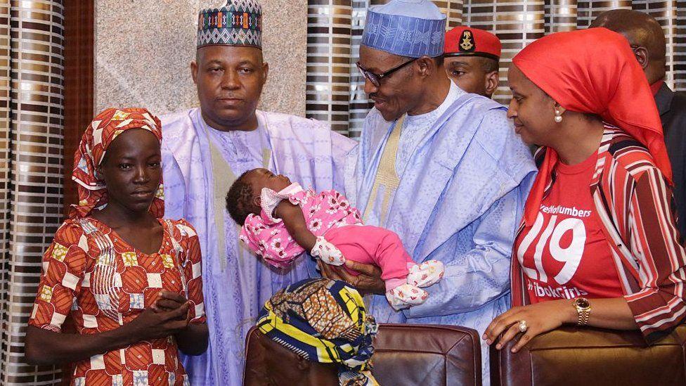 Nigerian President Mohammadu Buhari (C) flanked by Borno State governor Kashim Shettima (L) and Chief of Staff for the Kaduna State Governor Hadiza Bala Usman (R) carries Amina Ali's four-month-old baby on her arrival at the presidency in Abuja, on May 19, 2016
