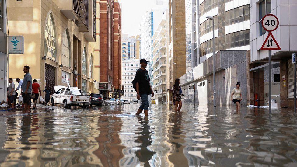 People walk through flood water caused by heavy rains in Dubai