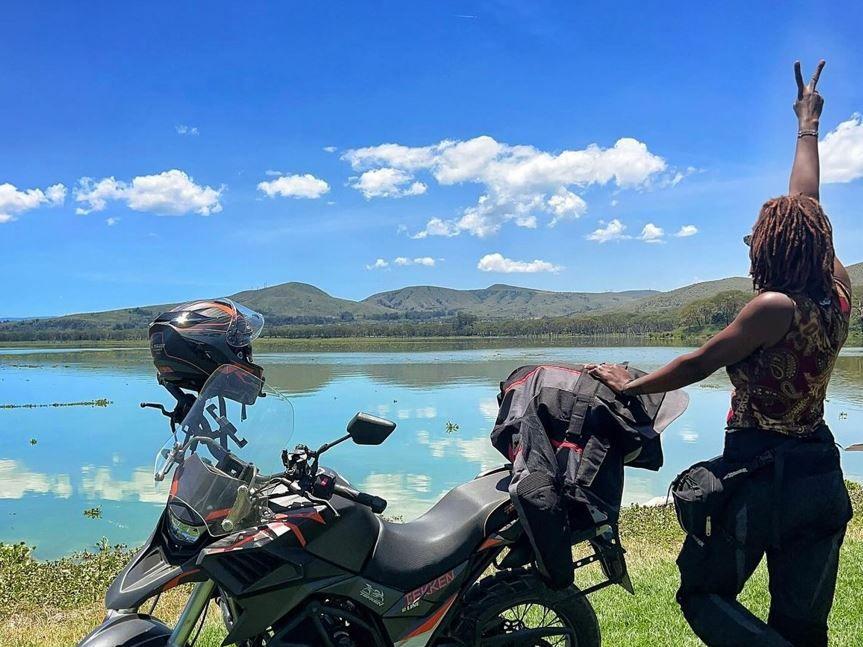 Udoh Ebaide Joy standing near her bike overlooking a beautiful lake situated at the bottom of a hill