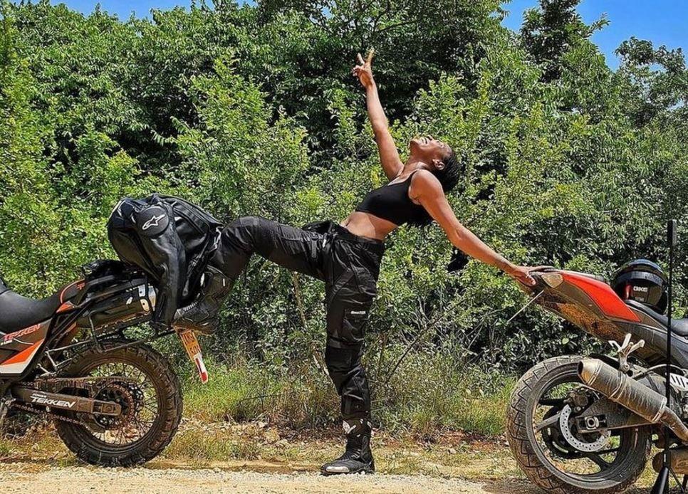 Ebaide standing between two bikes in a forested area and showing a victory sign 