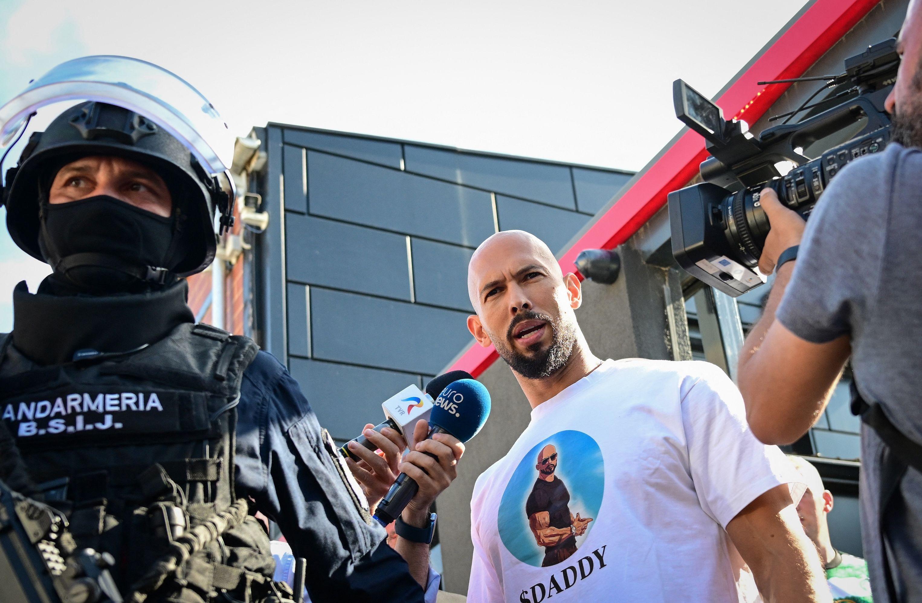 Andrew Tate (C), speaks to journalists as he is brought in for questioning by the Romanian gendarmes after a ten-hour long raid by police at their residency in Bucharest on August 21, 2024. 