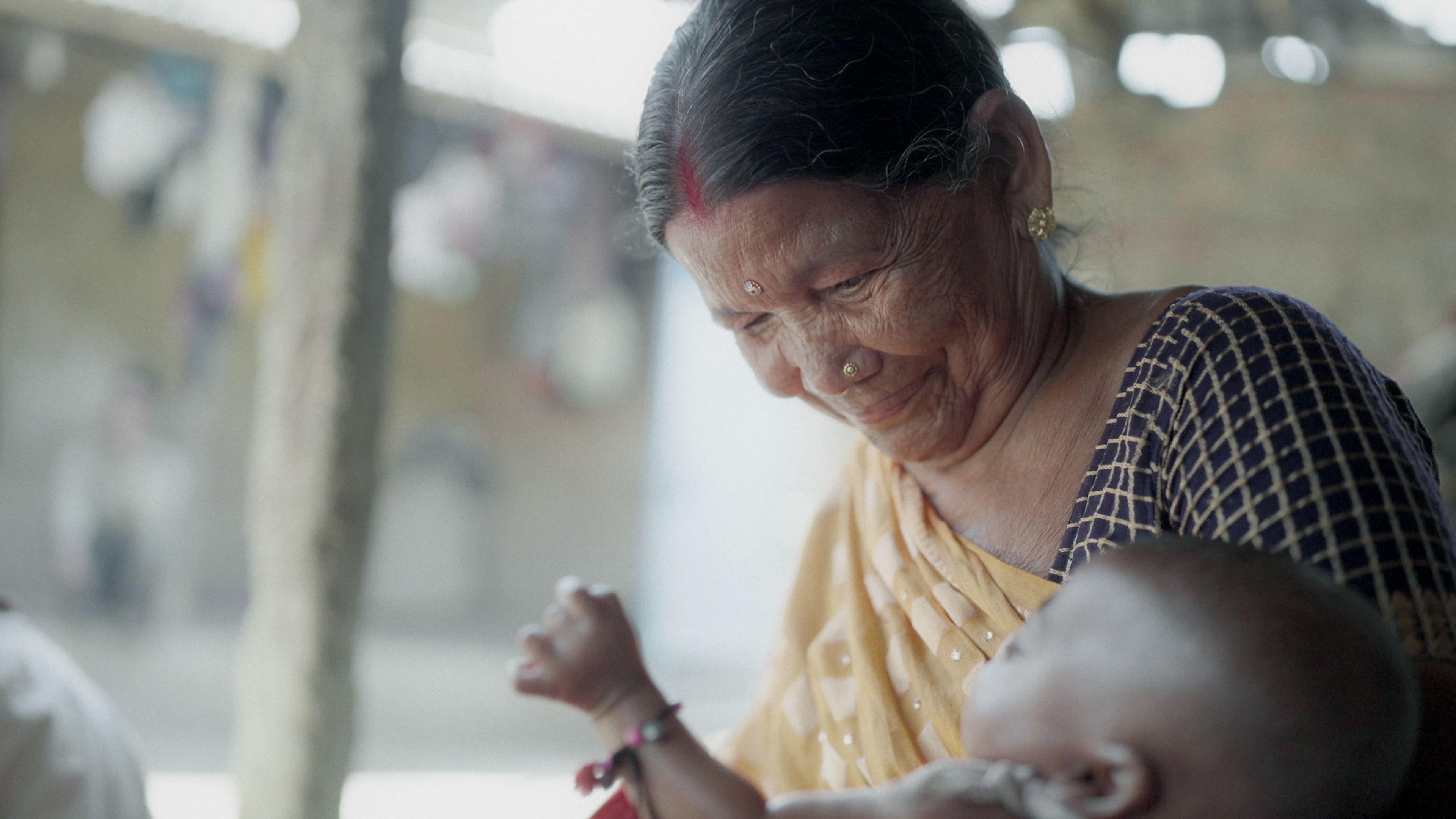 Siro na elderly woman, and she wear yellow sari, dey look one baby for her arms