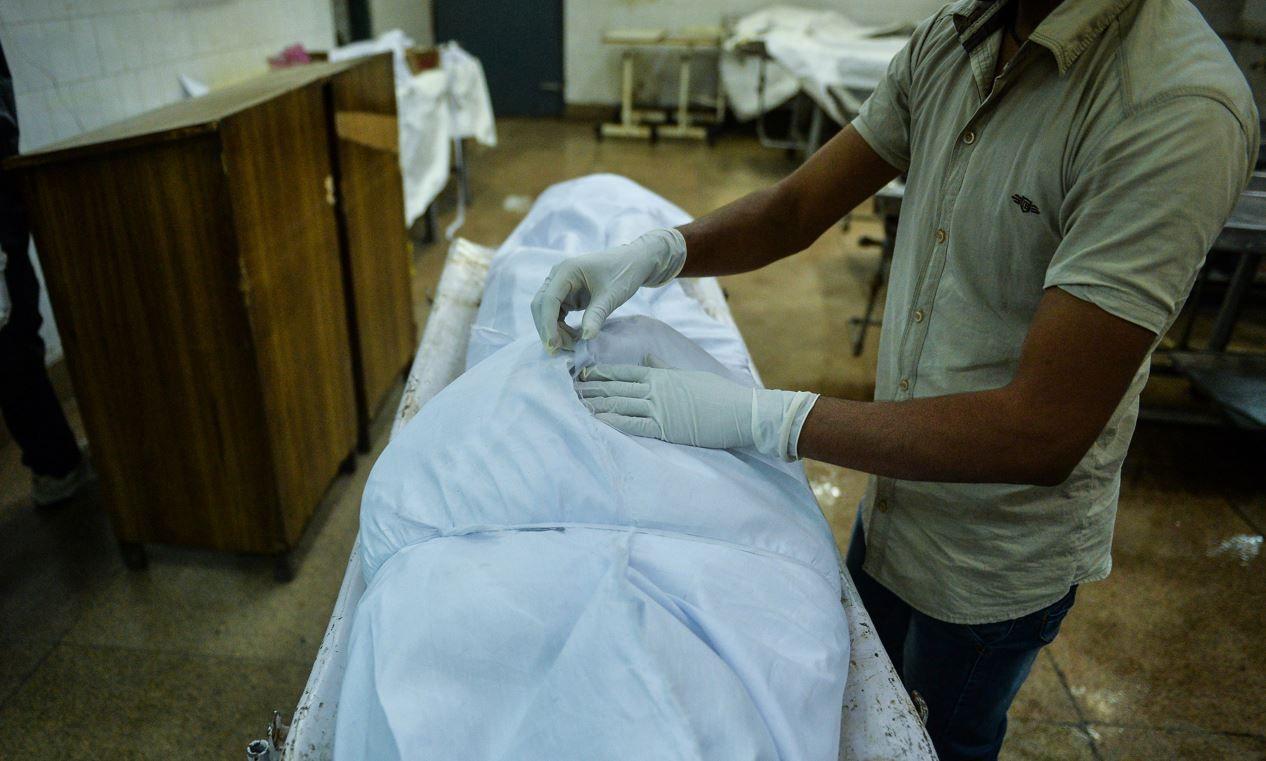 A mortician wrapping up a body in white cloth