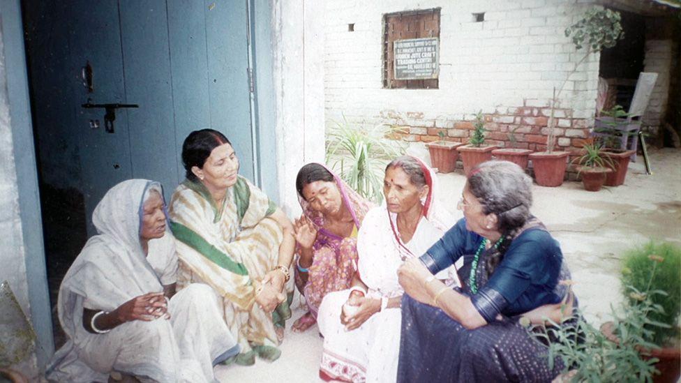 Anila, wear green, white and gold sari, dey listen as a group of midwives - all wey siddon for floor - tok to her. An archive photo from di 1990s.