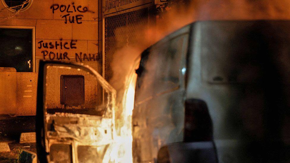 One van dey burn in front of a building with graffiti wey dem write in French 'Police kill' and 'Justice for Nahel' in Nanterre, France, one day after di killing of 17-year-old Nahel Merzouk - 28 June 2023