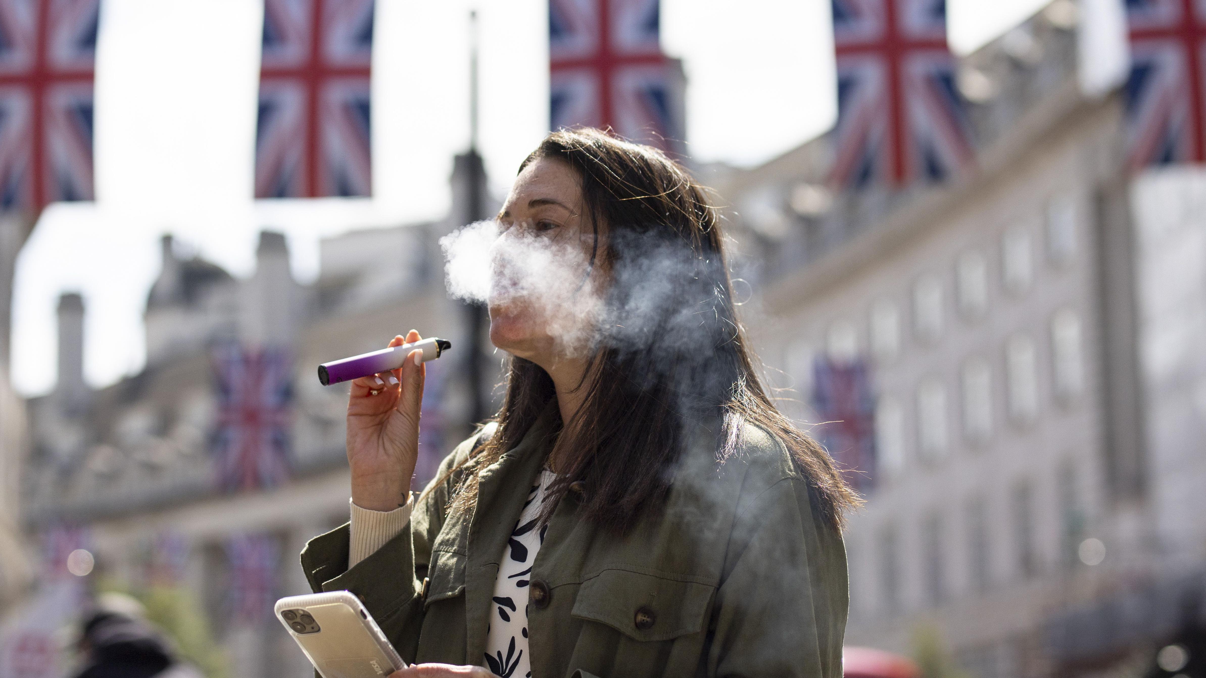 Woman wey dey smoke e-cigarette for central London, with union jack flags for di background