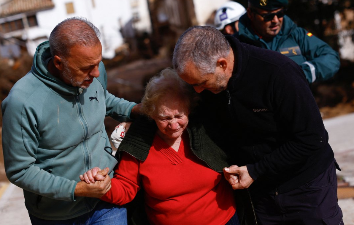 Two men support a woman who appears to be upset