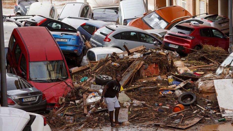 A man stands in front of rubble and cars in Valencia, Spain on 30 October 2024