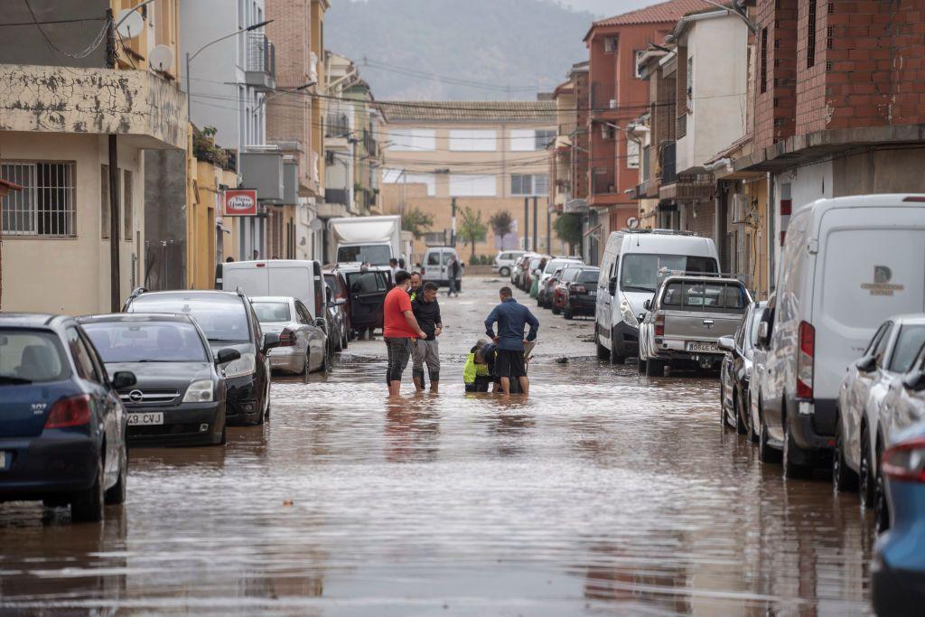 Men stand in a flooded street alongside someone in a high visibility jacket