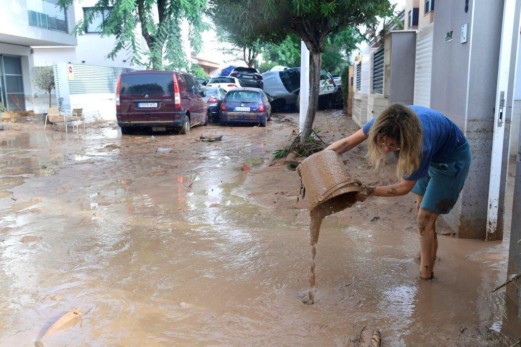 A woman empties  muddy water into the street from a bucket