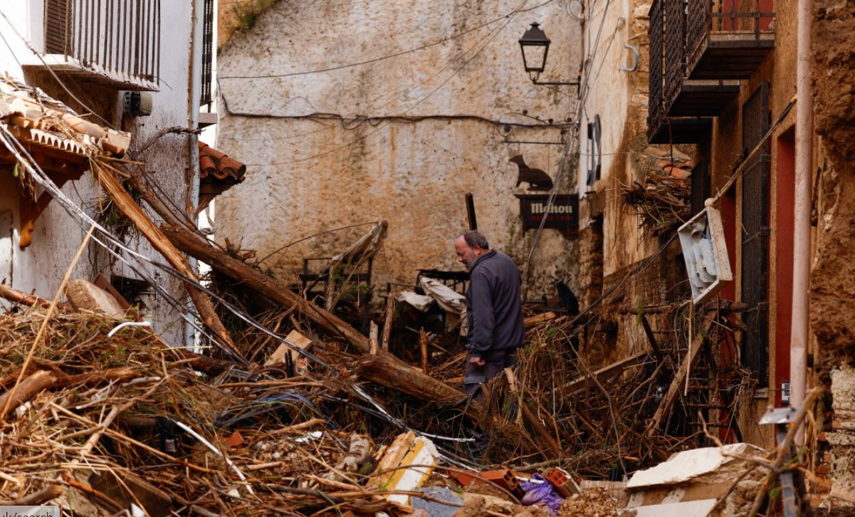 A man looks at a tree and wood beside three buildings