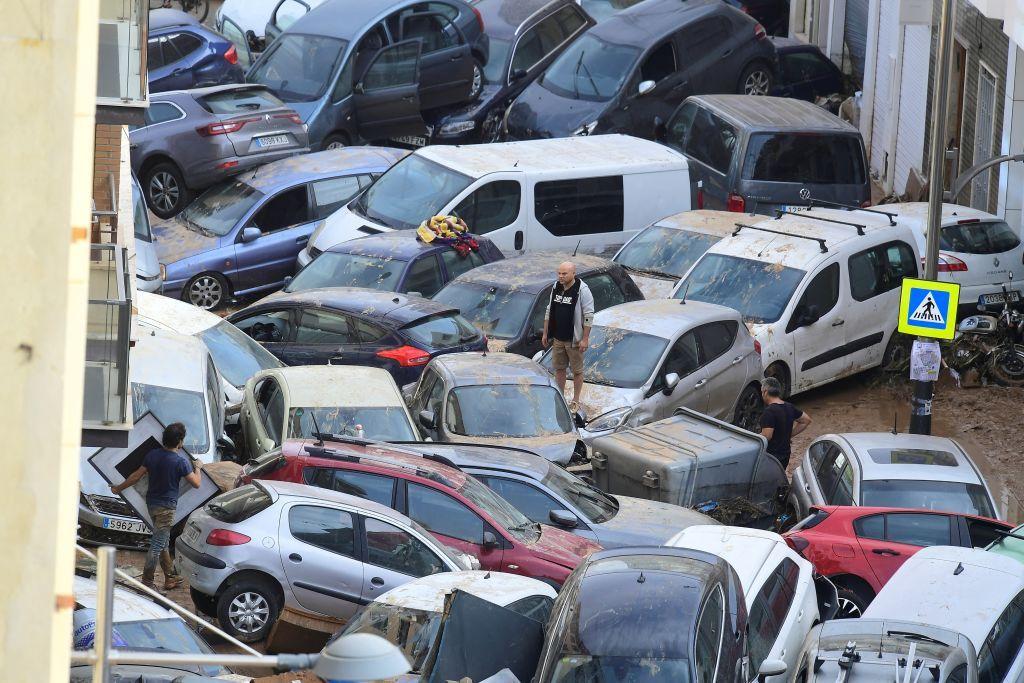 A man stands on the bonnet of a car among other vehicles that are stacked up on one another