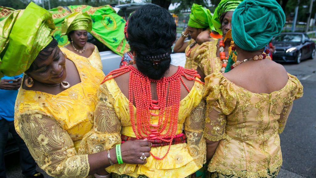 Texan African women put finishing touches to yellow and green fine clothing ready for a parade day celebrating their multiple cultures and heritage